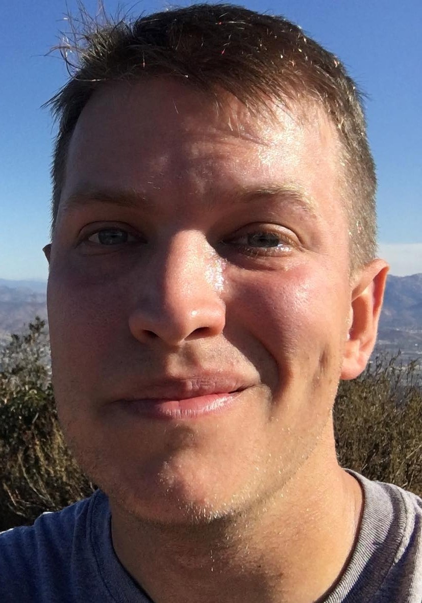 Photo of a gentleman smiling with mountains draped behind him.